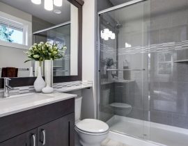 Bright new bathroom interior with glass walk in shower with grey tile surround, brown vanity cabinet topped with white counter and paired with mosaic tile backsplash. Northwest, USA